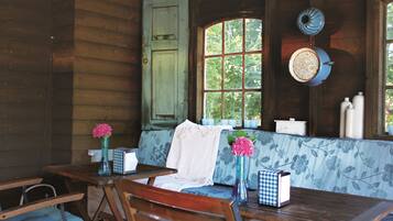 Interior de una cabaña de madera con comedor, un banco y una ventana con vistas a árboles.