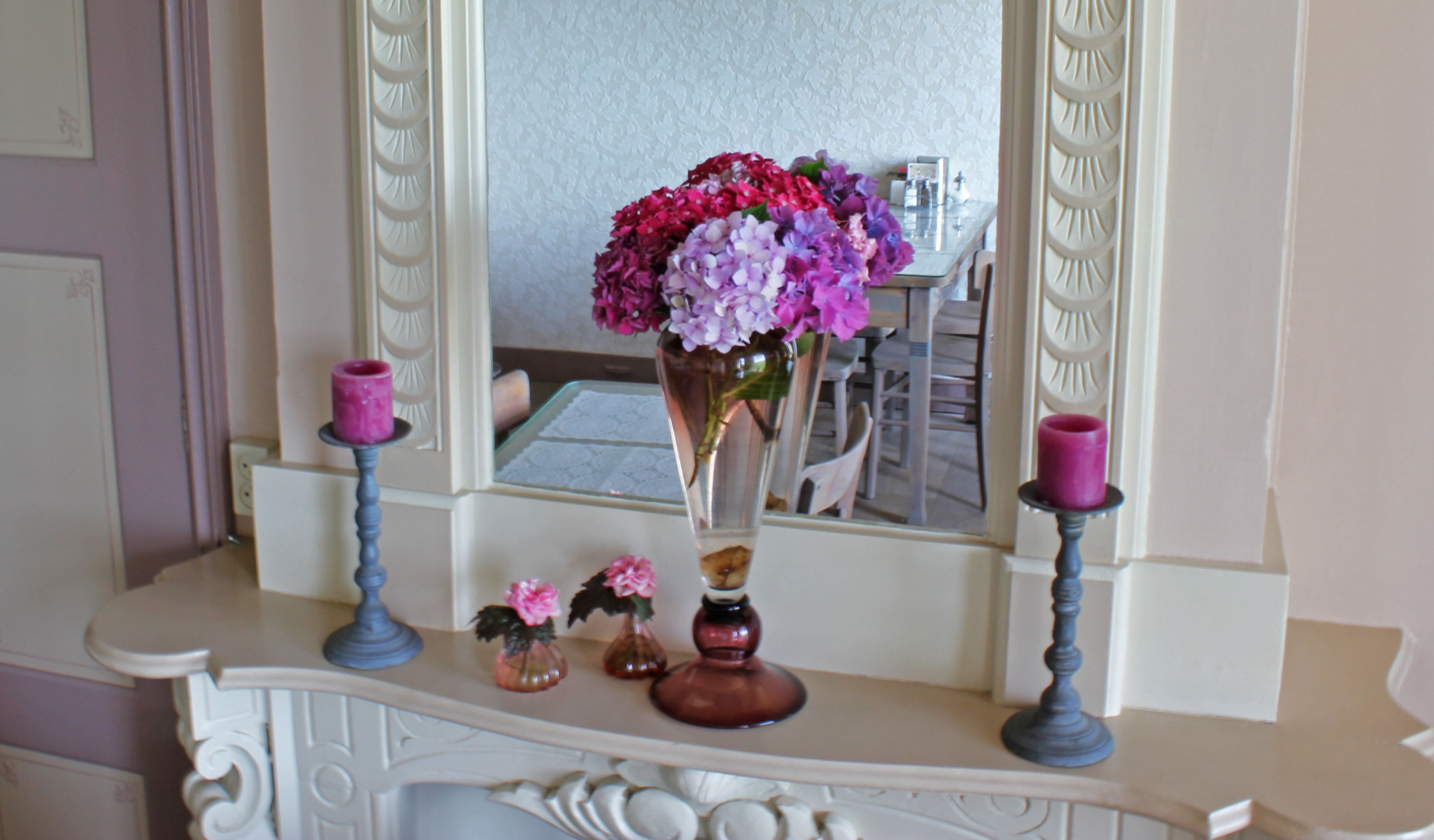 Une coiffeuse avec un miroir, un vase de fleurs et deux bougies posées dessus.