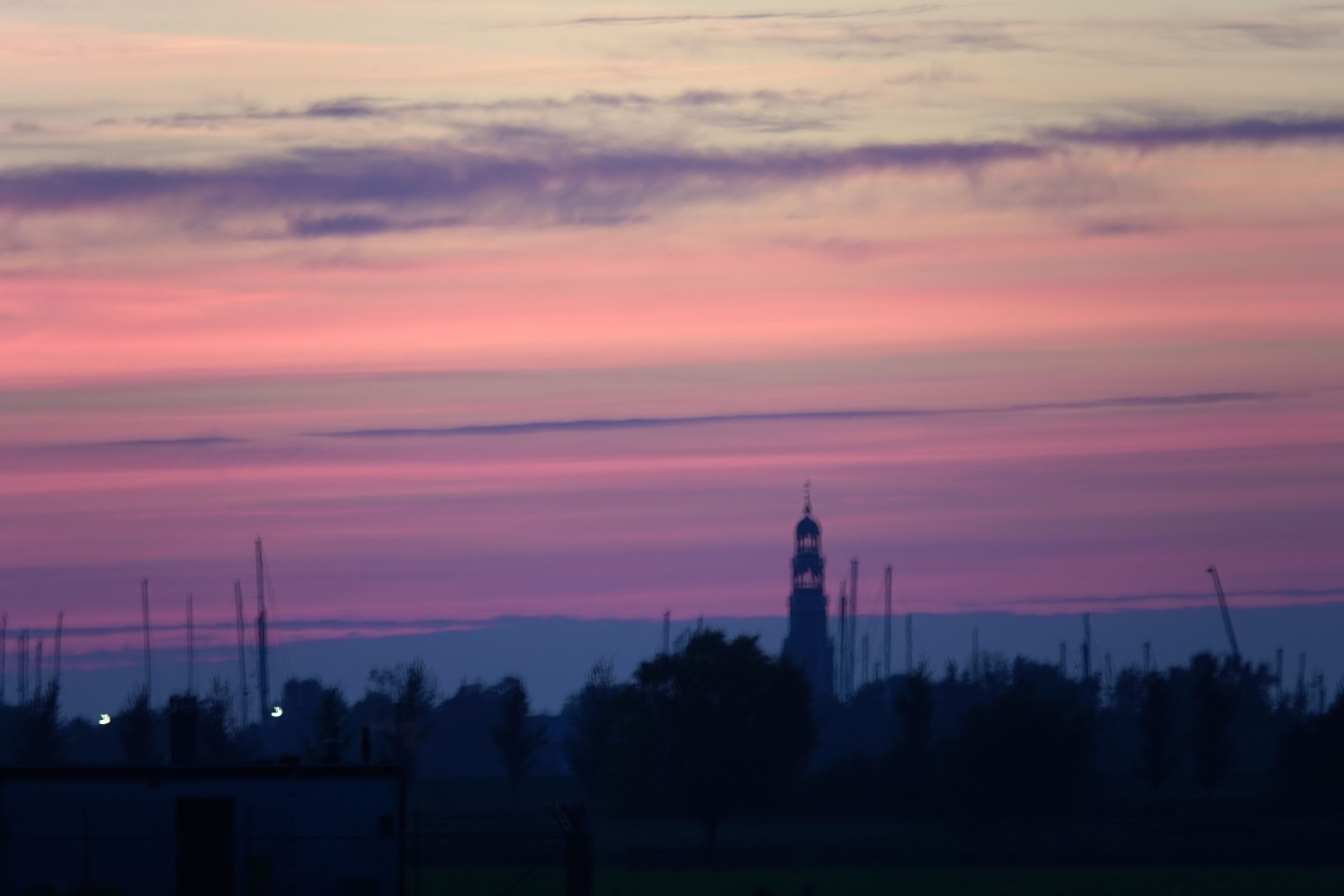 Eine Gebäude-Silhouette mit einem Turm, umgeben von Bäumen und offenen Feldern.