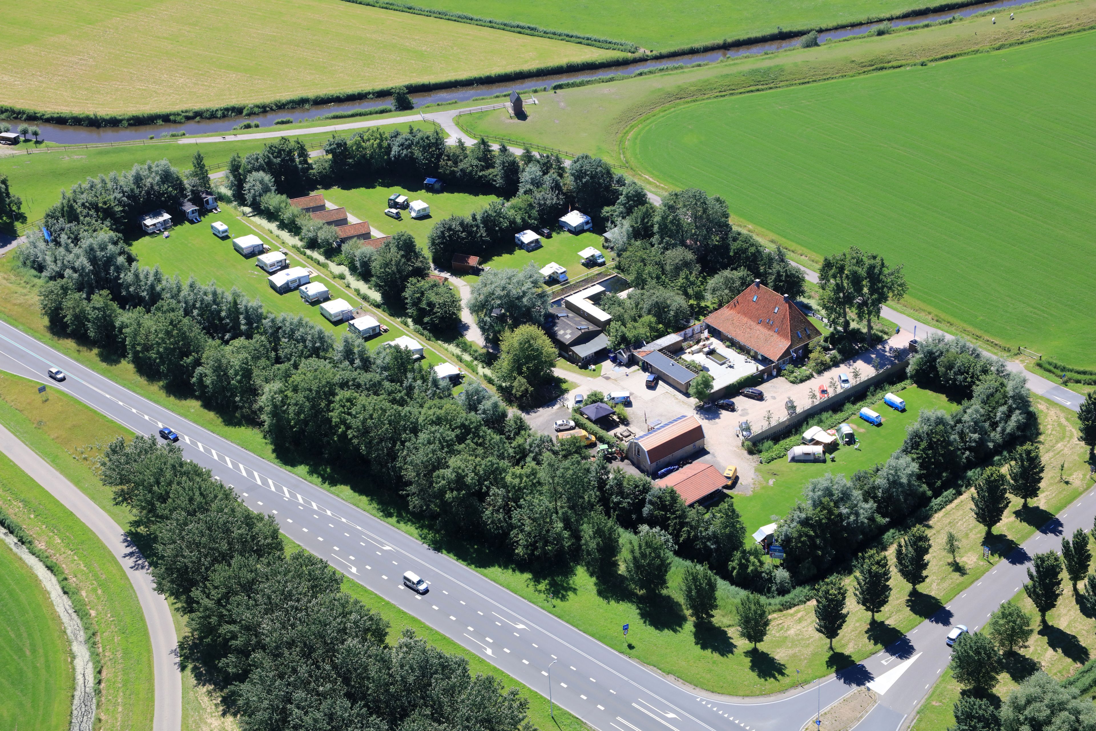 Luchtbeeld van een camping met meerdere tenten en blokhutten, omgeven door groen en een weg.