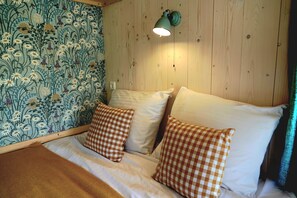 Ein Zimmer mit Holzvertäfelung, einem Bett, karierten Kissen und floralem Wandpapier.