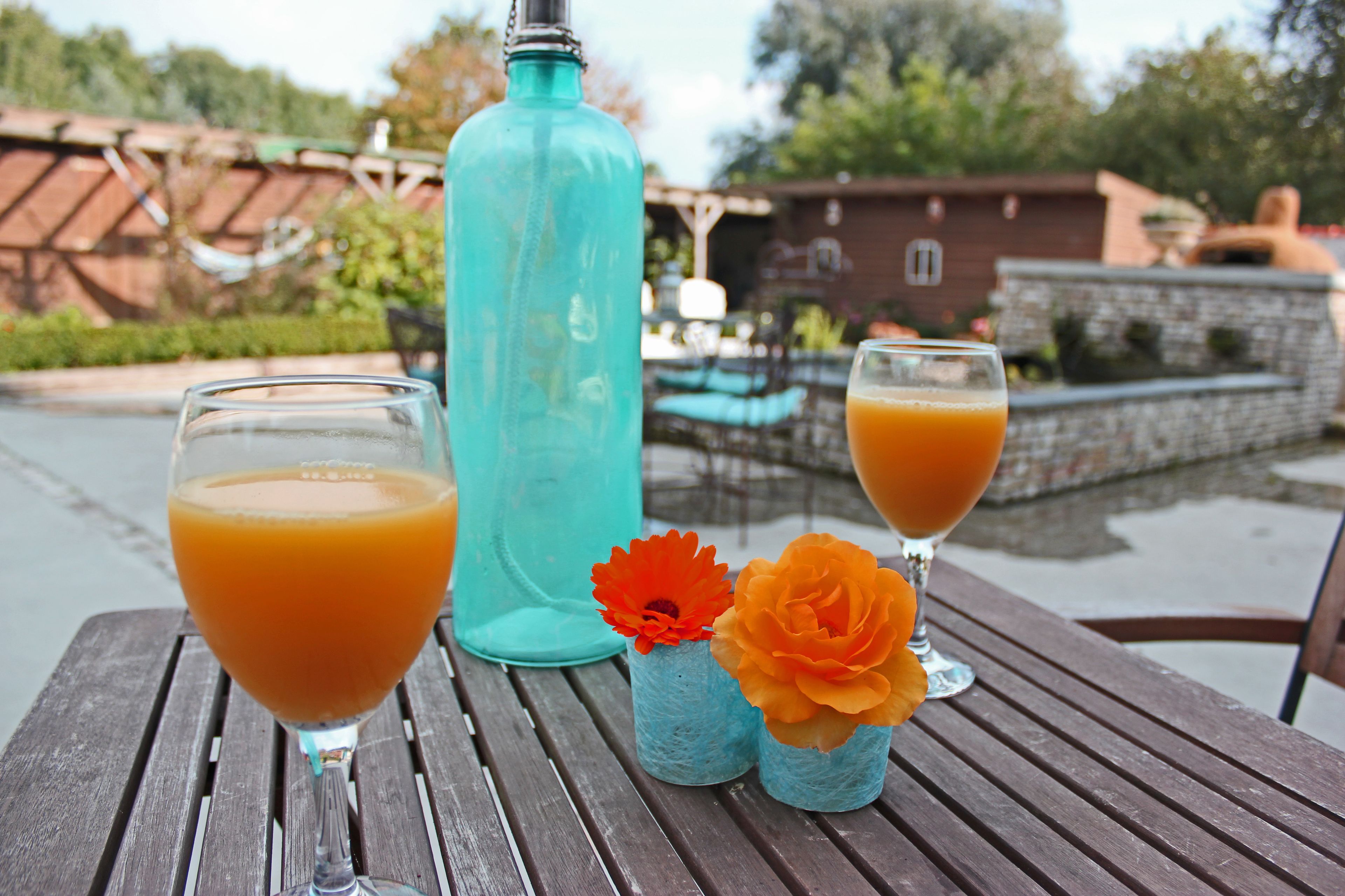 Een houten tafel met twee glazen sinaasappelsap en een turquoise fles.