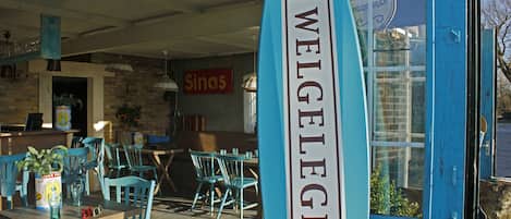 Ein Außenbereich mit blauen Stühlen und einem Schild mit dem Aufdruck "WELGEGEN" in Surfbrett-Optik.