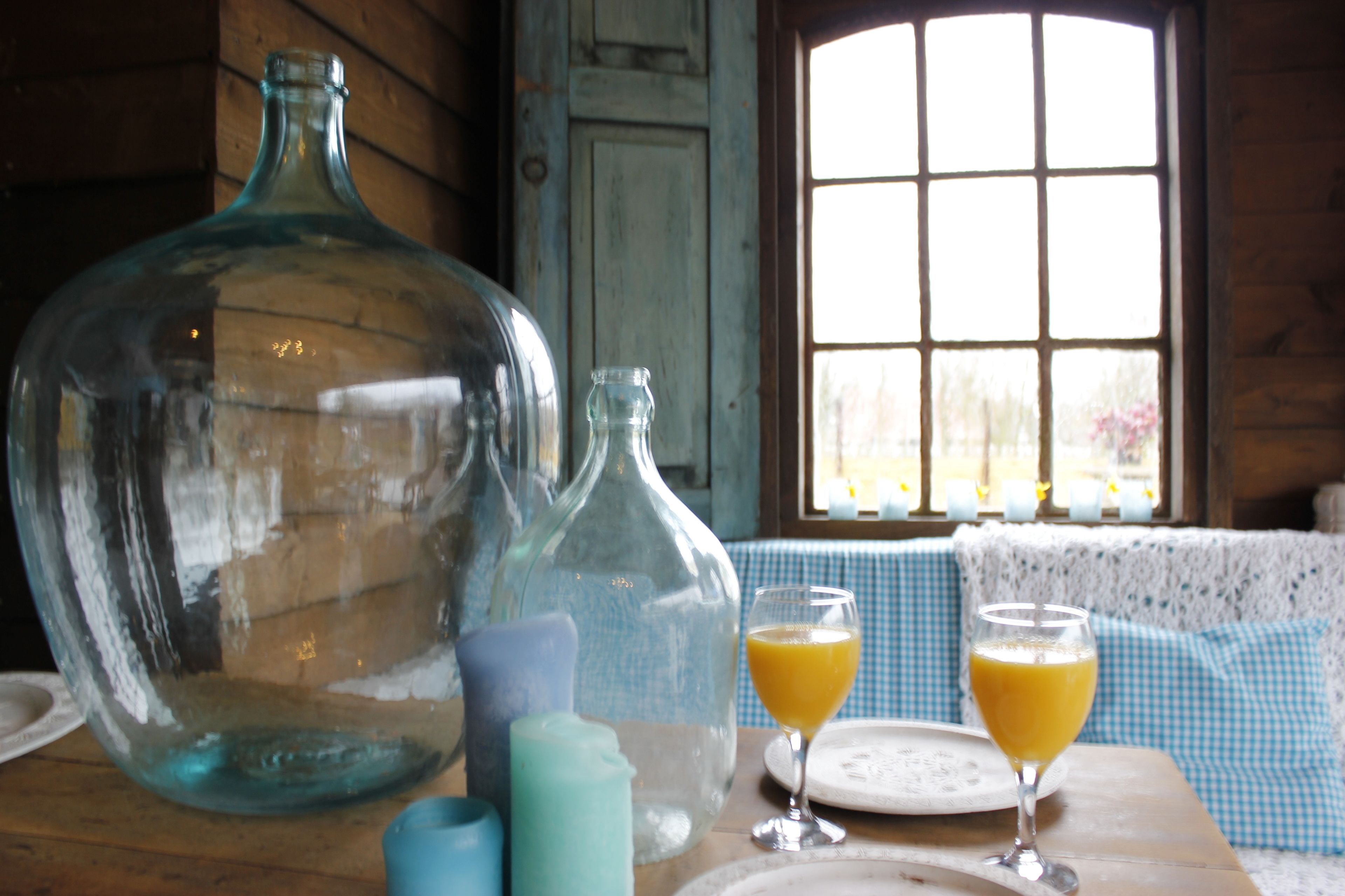 Et træbord med en stor glasvandkaraffel, en mindre glasflaske og to glas appelsinjuice.