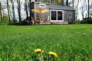 A small wooden cabin with a patio, a table, and chairs, surrounded by a grassy field and trees. - B&B en camping Welgelegen (Workum)