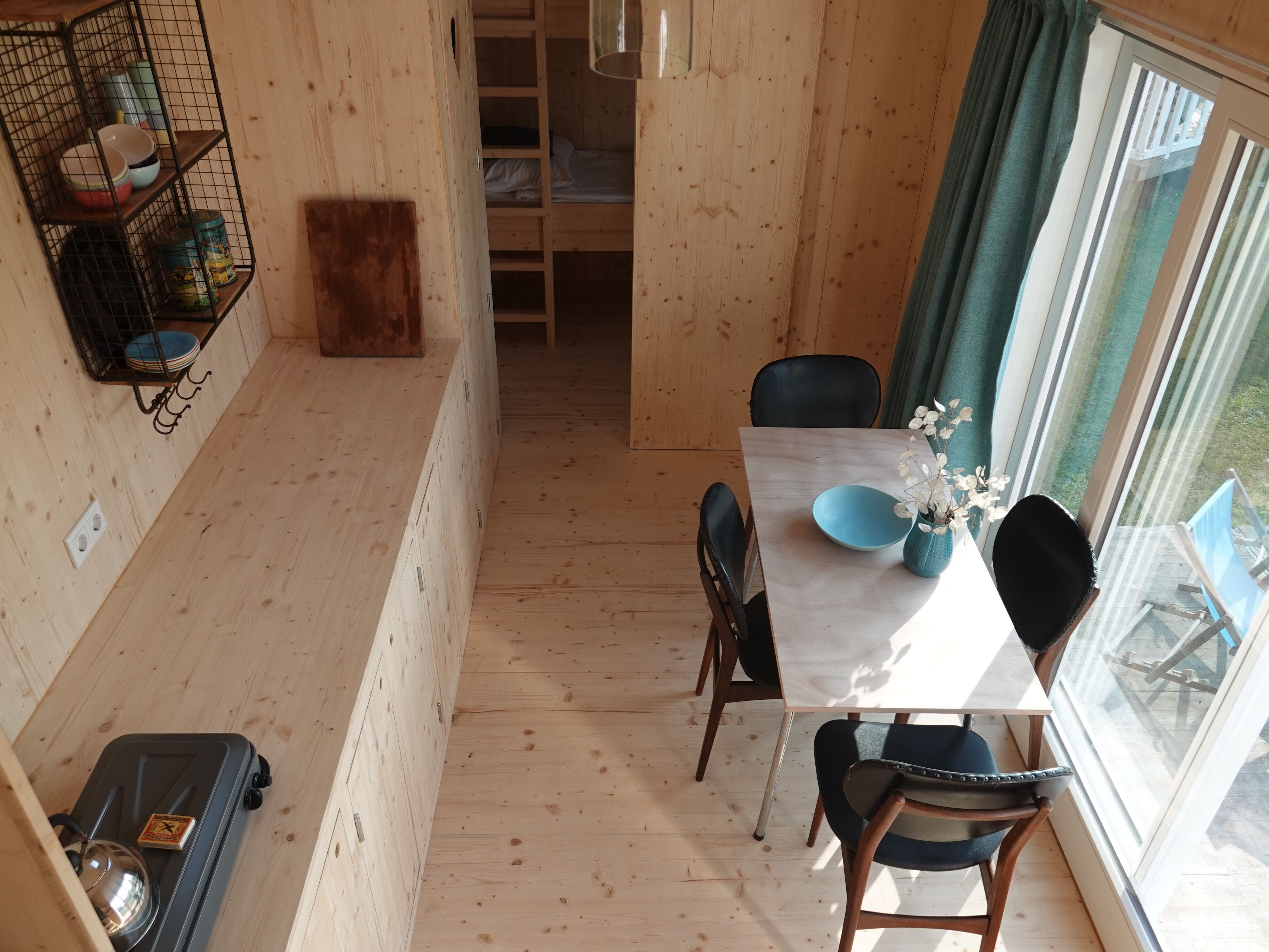 Ett litet, kompakt rum med träinredning, ett matbord, stolar, ett litet pentry och ett fönster med gardiner.