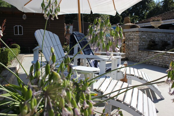 Un patio con sillas Adirondack blancas, una mesita y un muro de piedra.