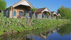 Una hilera de cabañas de madera frente a un estanque, rodeadas de abundante vegetación.