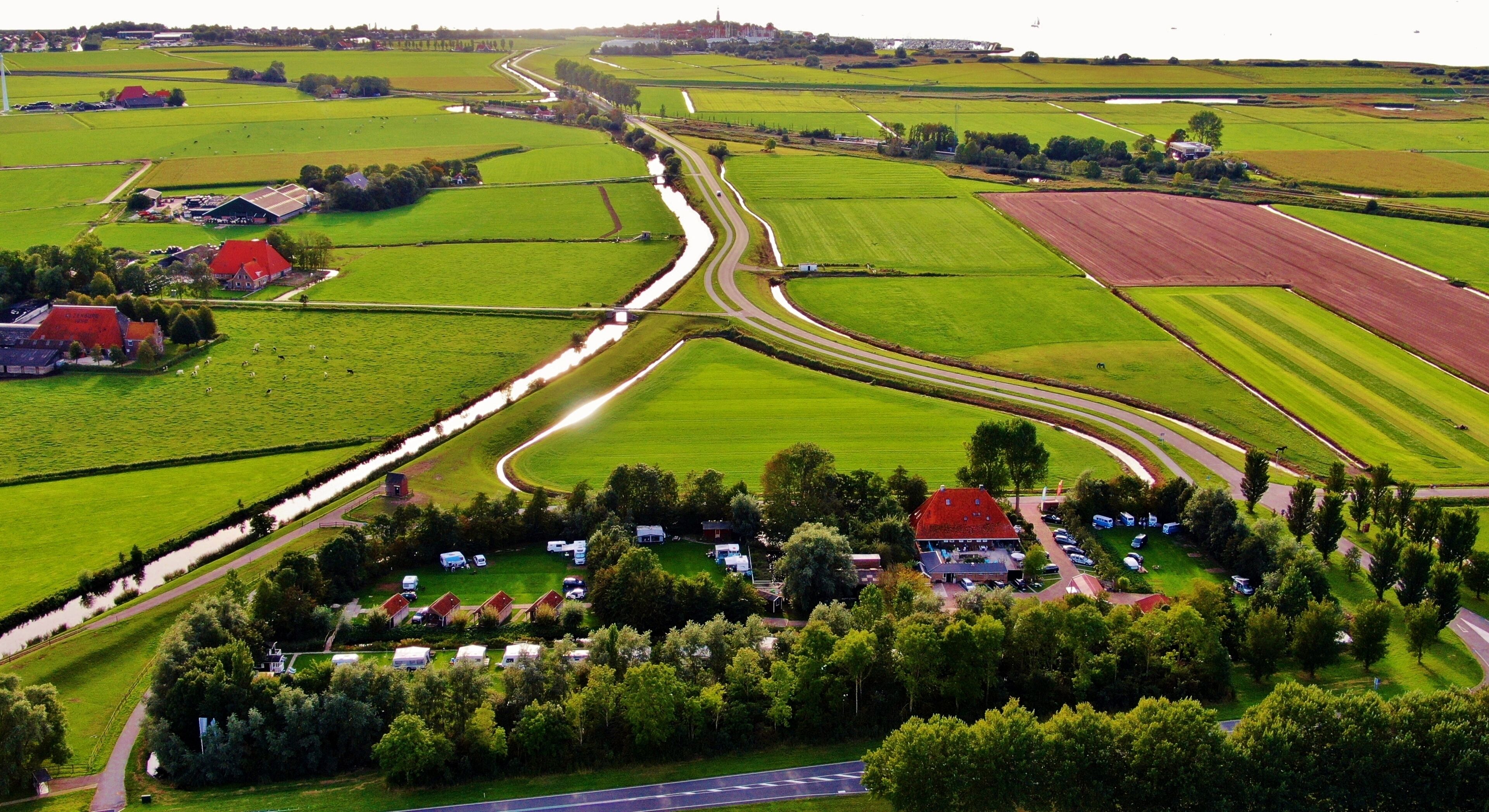 Vista aérea de una zona rural con campos, una carretera sinuosa y un conjunto de edificios con tejados rojos.