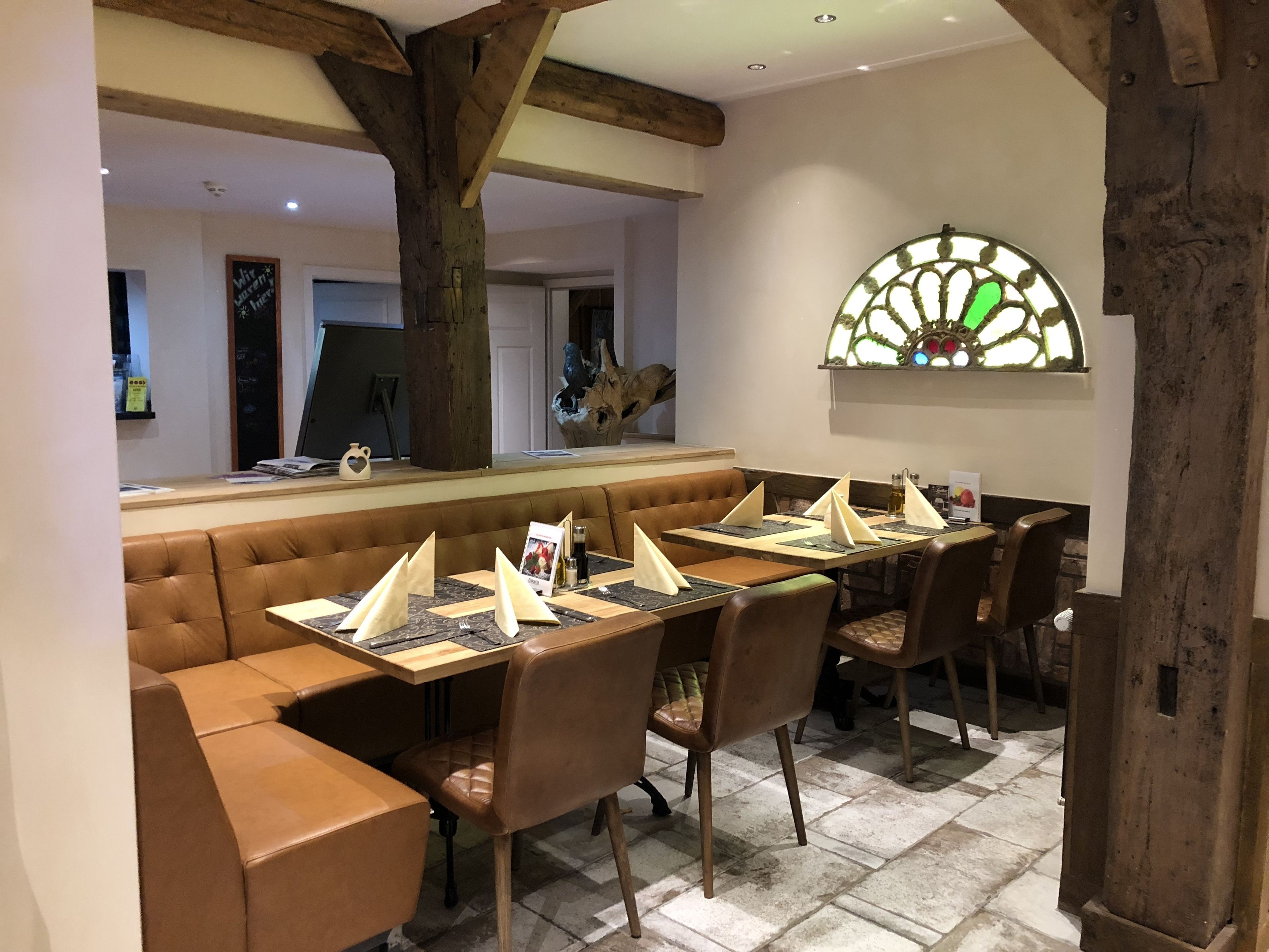 A restaurant with a long wooden table set for a meal, cushioned seating, and a decorative stained glass window.