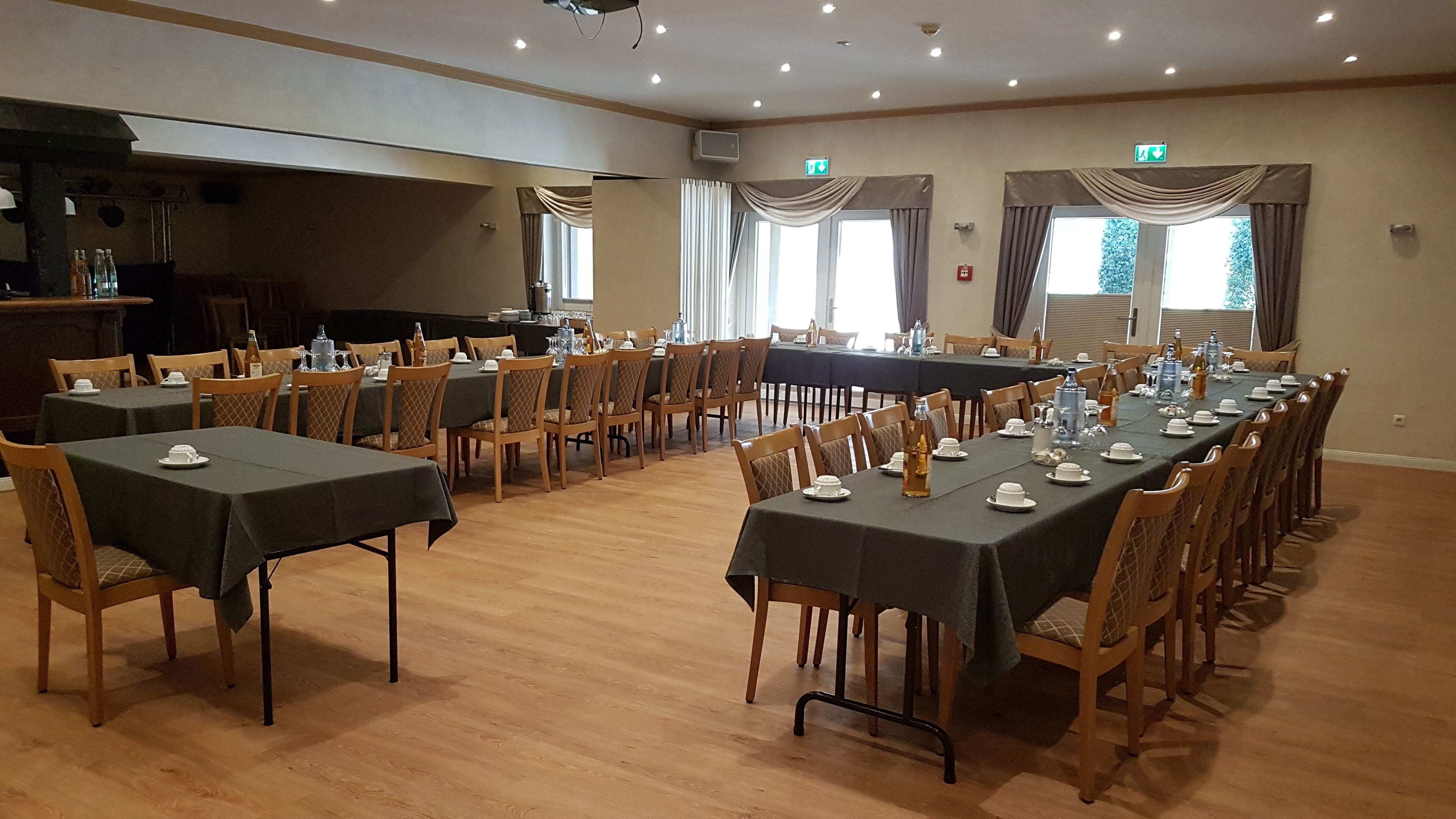 A conference room with multiple tables set for a meeting, equipped with chairs and tables, and large windows with curtains.