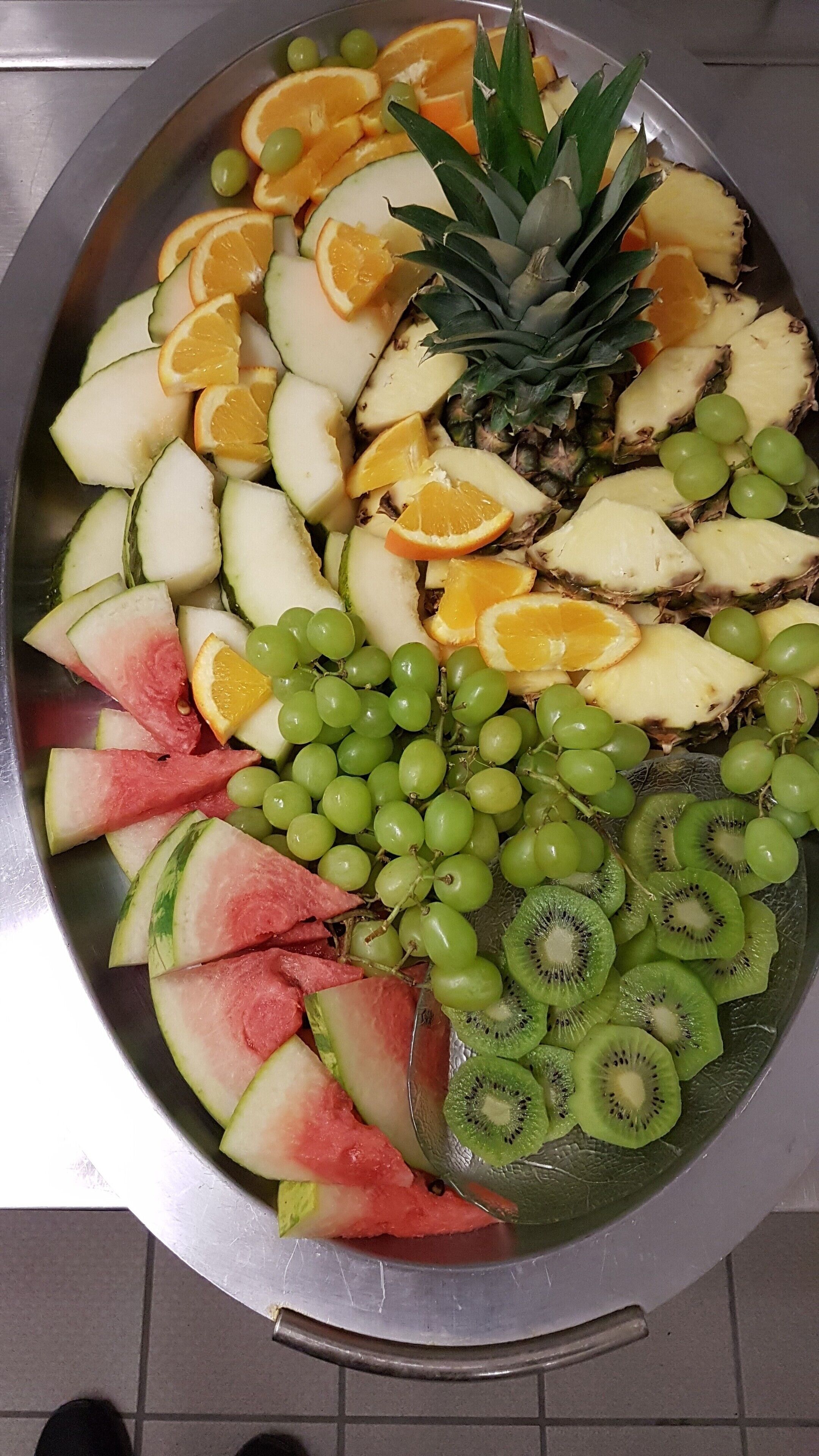 Una bandeja metálica grande llena de frutas variadas, como sandía, kiwi, uvas, piña y naranjas.