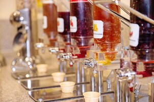 Un dispensador de bebidas con varios grifos, cada uno con etiqueta y un recipiente transparente debajo.
