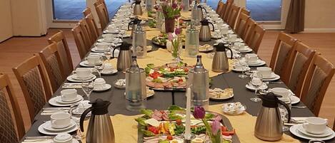 A long conference table set for a formal event with multiple chairs, a floral centerpiece, and various dishes and drinks.