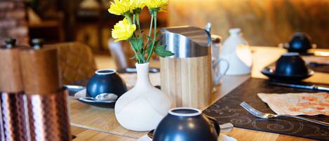 Una mesa de comedor dispuesta con diferentes pots de té y tazas, un florero con flores amarillas y una jarra de madera.