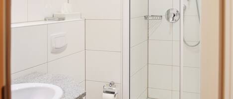 Un baño moderno con ducha de vidrio, inodoro blanco y lavamanos de granito.