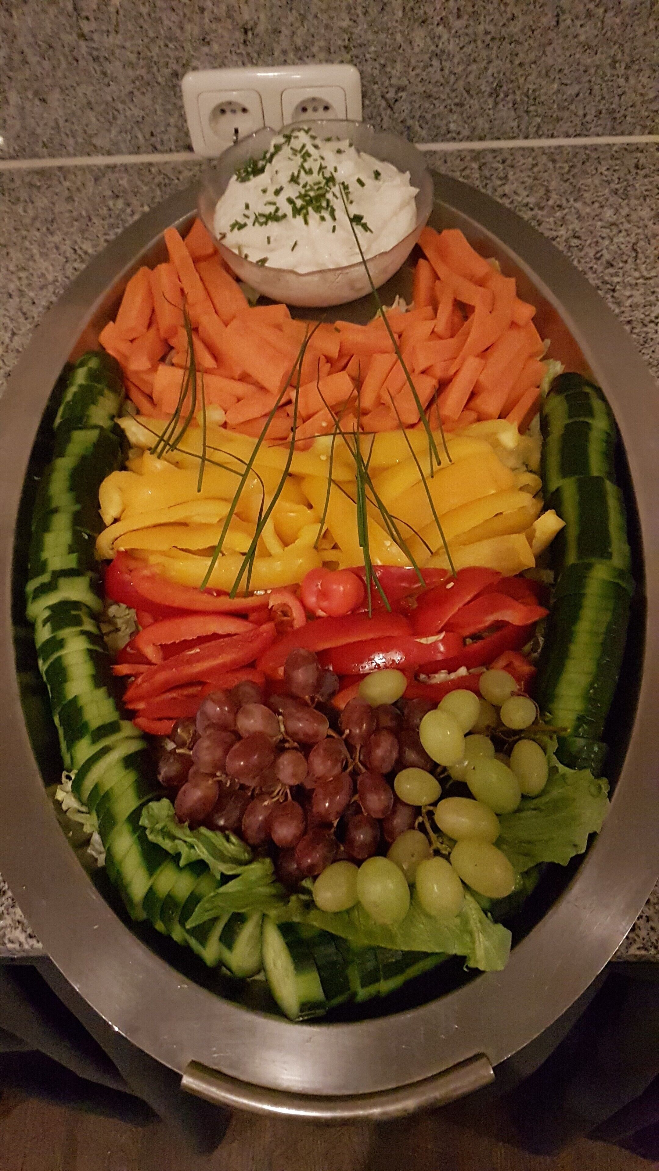 A platter of assorted vegetables and a bowl of dip on a granite countertop.
