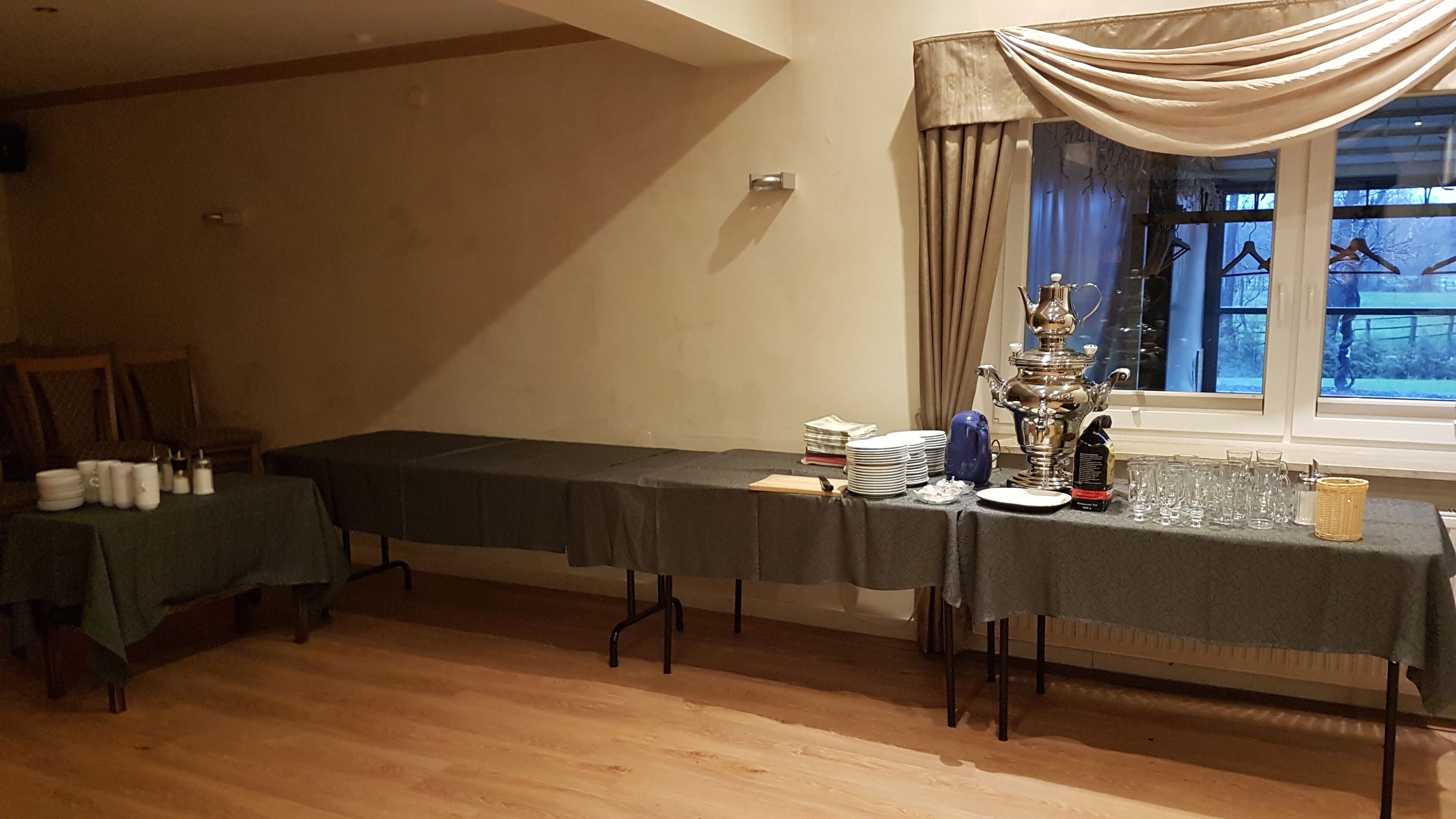 Un comedor con una mesa larga dispuesta para una comida, un ornamentado jarro de plata y vistas al exterior a través de una ventana.