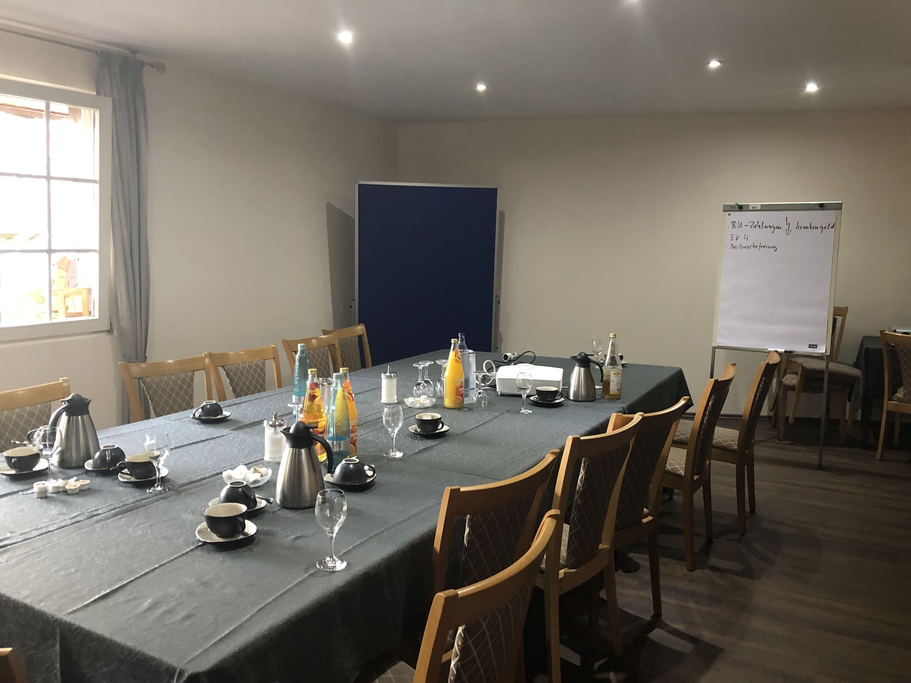 A conference room with a long table set for a meeting, equipped with chairs, a projector, and a whiteboard.