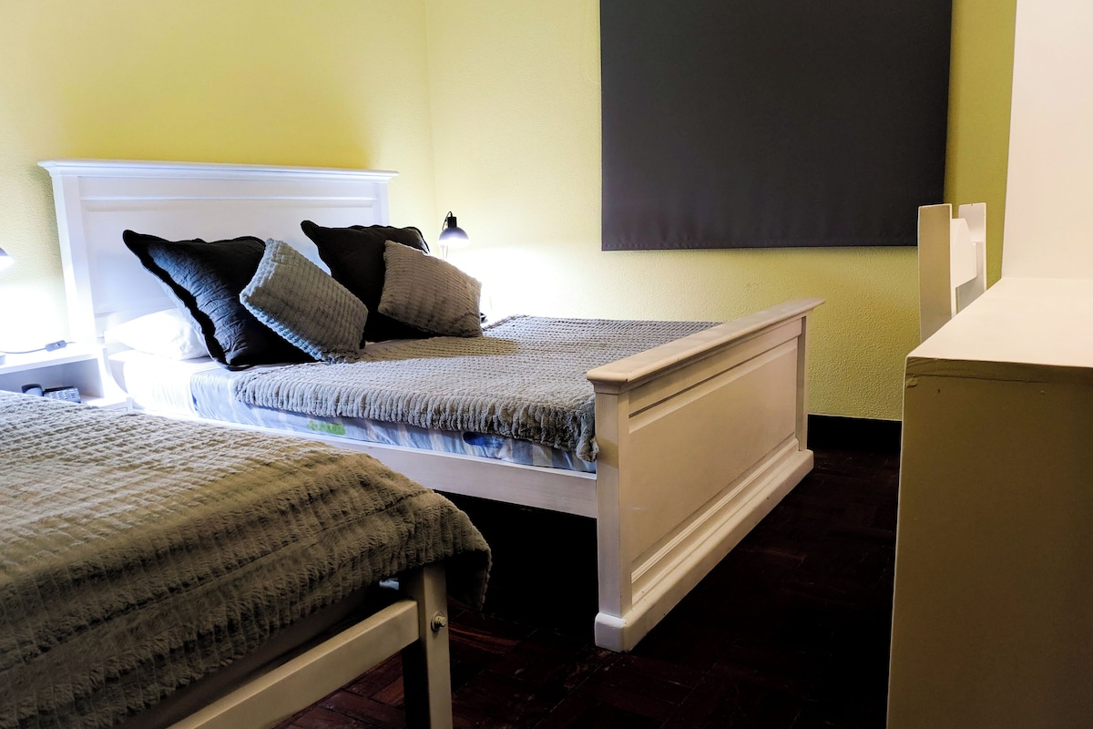 A bedroom with two single beds, a nightstand with a lamp, and a wall-mounted TV.