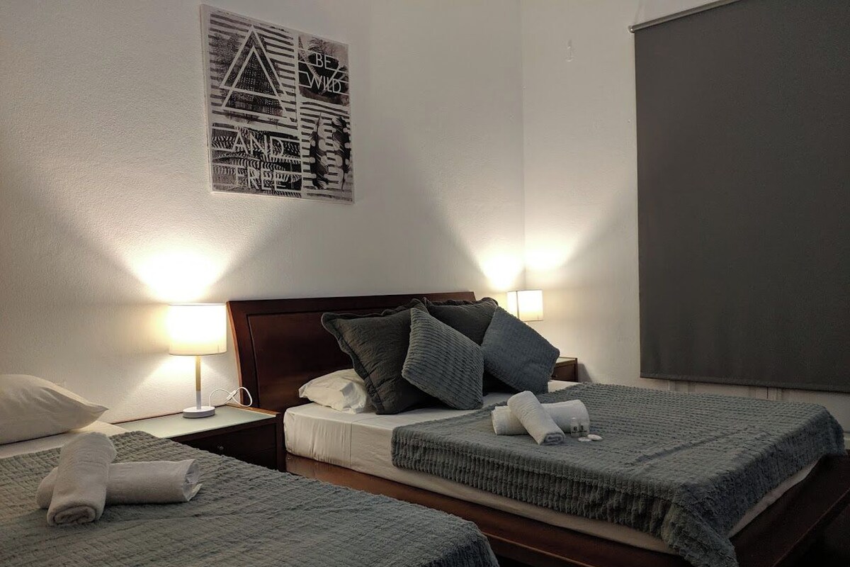 A hotel room with two beds, each with a grey blanket and pillows, a wooden headboard, and a wall-mounted light fixture.