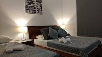Una habitación de hotel con dos camas, cada una con una manta gris y almohadas, un cabecero de madera y una lámpara fijada a la pared.