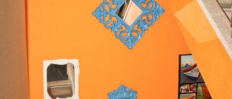 Una escalera con una pared naranja, un marco decorativo azul y una ventana pequeña.
