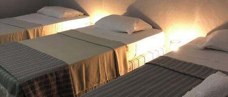 A hotel room with two single beds, each with a pillow and a blanket. There is a framed picture on the wall above the beds.