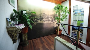 A room with a wooden floor, a large window with a view of a coastal landscape, and two potted plants. - Residencial Funchal (Funchal)