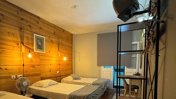 A hotel room with two single beds, a wooden wall, a ceiling fan, and a small table with a lamp. - Residencial Funchal (Funchal)