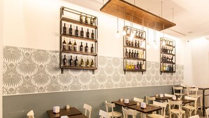 A restaurant interior with multiple tables and chairs, wooden shelves with bottles, and patterned wallpaper. - El Dorado Vatican (Rome)