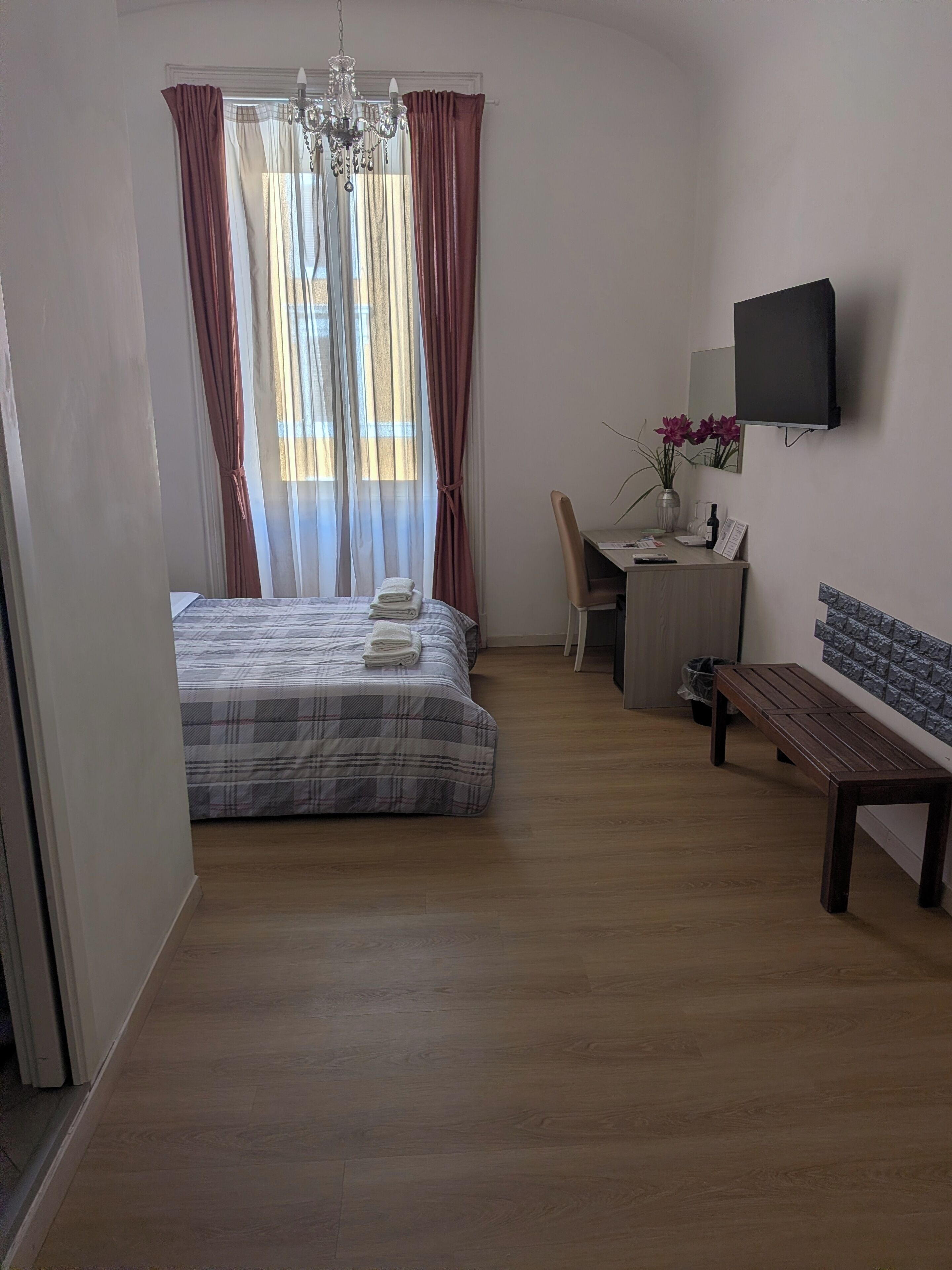 Un dormitorio con cama, escritorio, silla, banco y televisor en la pared.