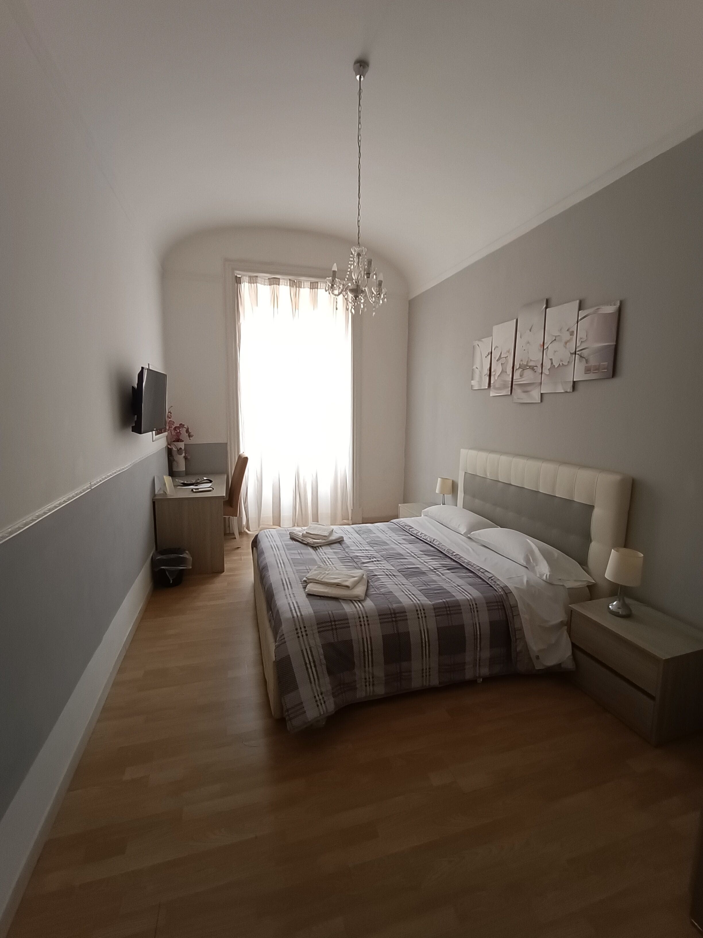 Un dormitorio con cama, mesitas de noche, televisión y obras de arte en la pared.