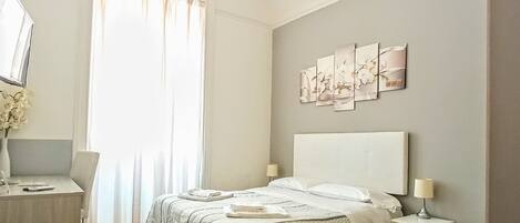 A bedroom with a bed, bedside tables, a desk, and a chandelier.