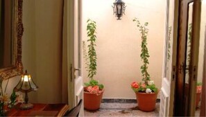 Un couloir avec deux plantes en pot, un luminaire fixé au mur et un miroir sur le côté gauche.