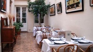 Un comedor con mesas dispuestas para el servicio, una planta en maceta y cuadros en la pared.