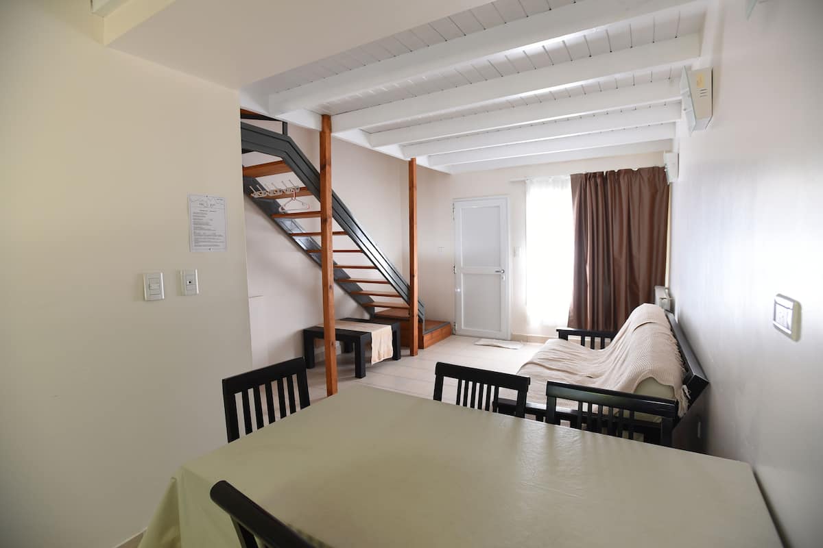 Une pièce comprenant une table à manger, des chaises, un escalier, un lit et une porte.