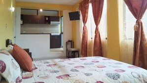 A bedroom with a bed, a small kitchenette, a TV, and curtains. - Chez Elena Guesthouse (Quito)