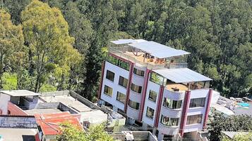 Un edificio de varios pisos con terraza en la azotea, rodeado de un bosque denso.