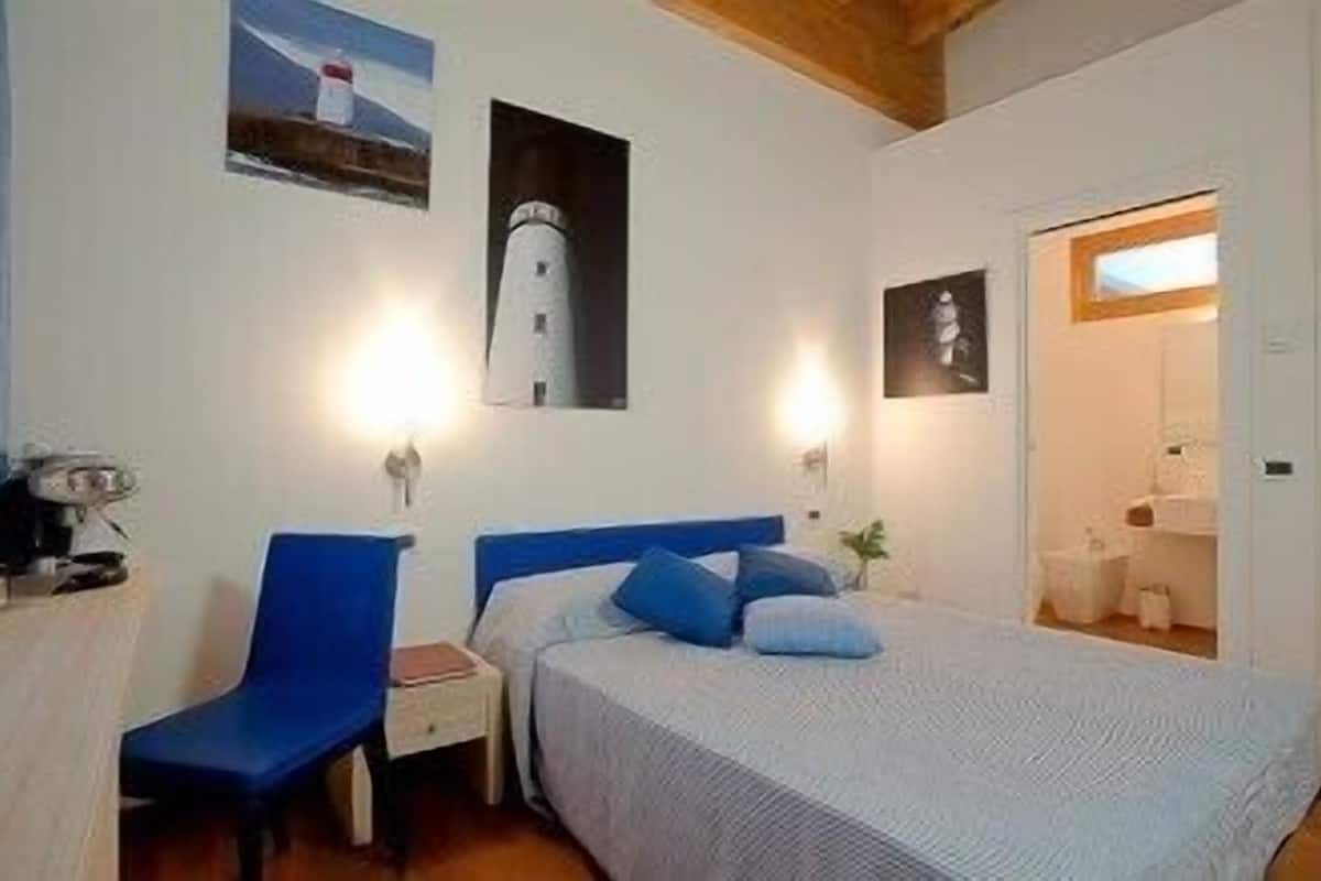 A bedroom with a bed, a chair, a nightstand, and a wall-mounted lamp.