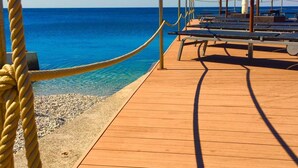 Una terraza de madera con barandillas de cuerda, sombrillas blancas y una vista despejada al mar.