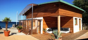 A wooden cabin with a covered patio, a view of the sea, and outdoor seating. - Tre Merli Beach Hotel (Trieste)