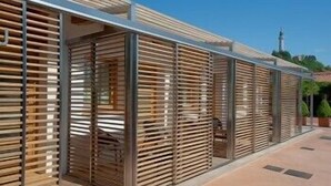 Un edificio moderno con varios espacios cerrados, que podrían ser habitaciones de huéspedes o suites, con listones horizontales de madera y estructuras metálicas.