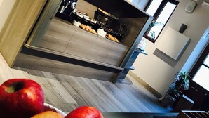 Una cocina moderna con horno integrado y un comedor con sofá oscuro. Hay manzanas y limones en la encimera.
