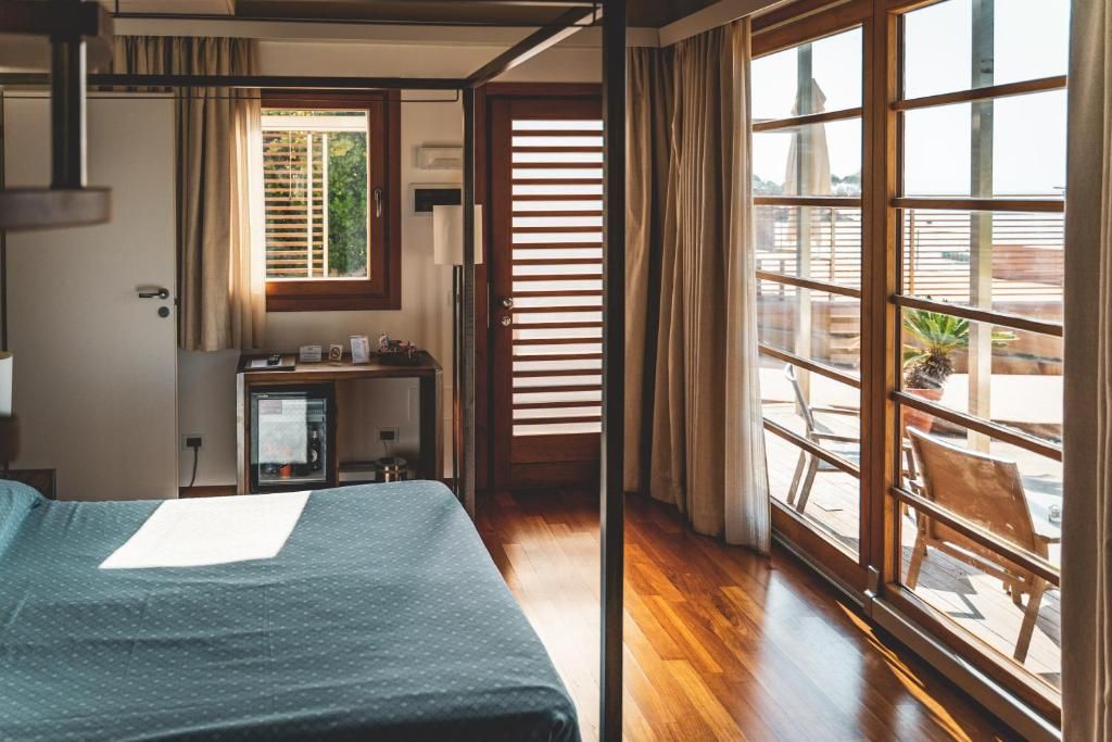 A hotel room with a bed, a desk with a computer, a window with blinds, and a view of the outdoors.