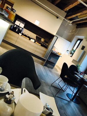 A modern kitchen with a built-in stove, a dining area with a black chair, and a small table with a cup and saucer. - Tre Merli Beach Hotel (Trieste)