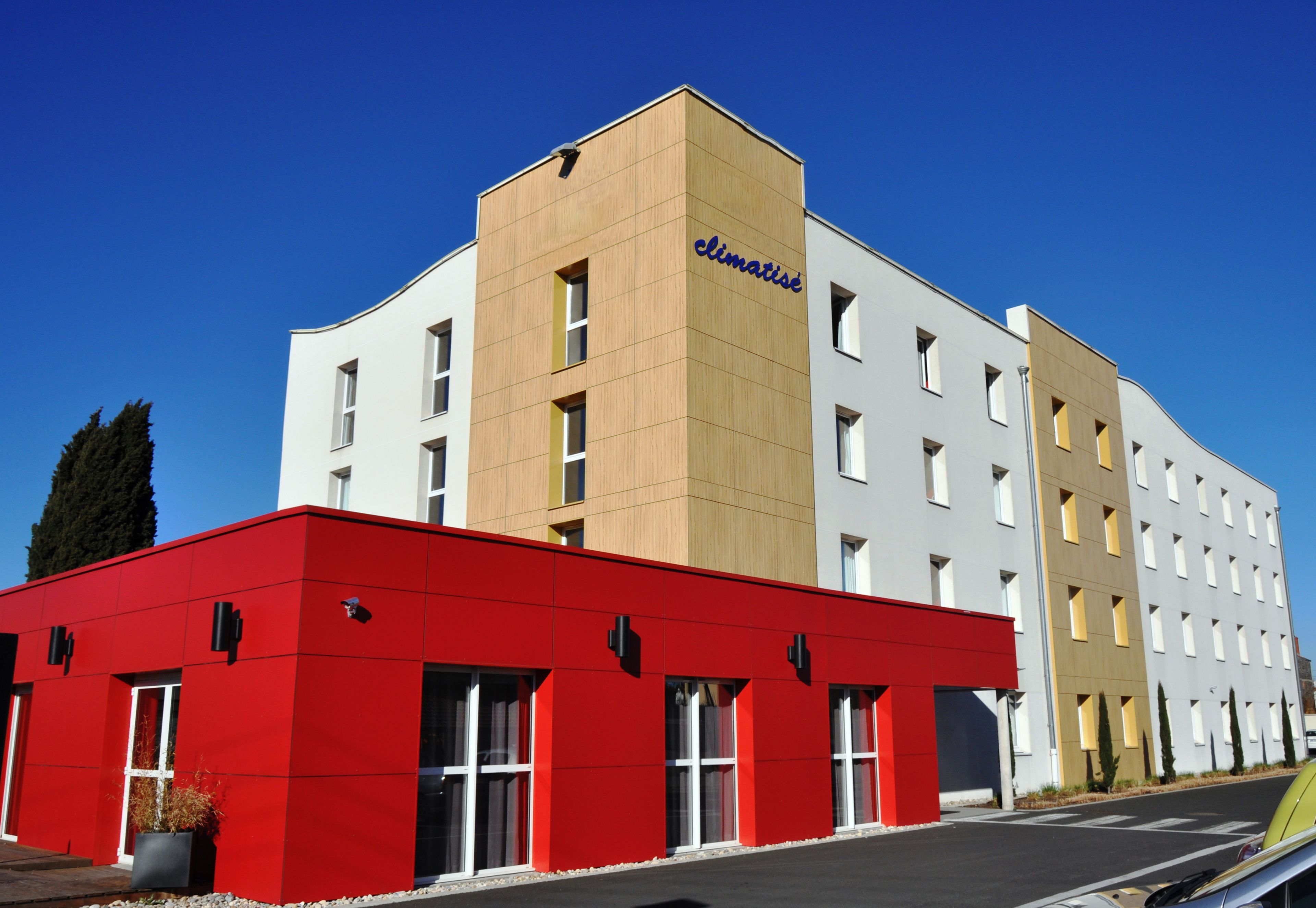 Ein modernes Hotel mit roter und weißer Fassade, zahlreichen Fenstern und blauem Himmel.