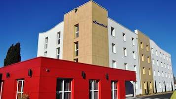 A modern hotel with a red and white facade, multiple windows, and a clear sky.