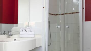 Un baño moderno con ducha envuelta en vidrio, un lavamanos blanco con toallero y una pared de acento roja.