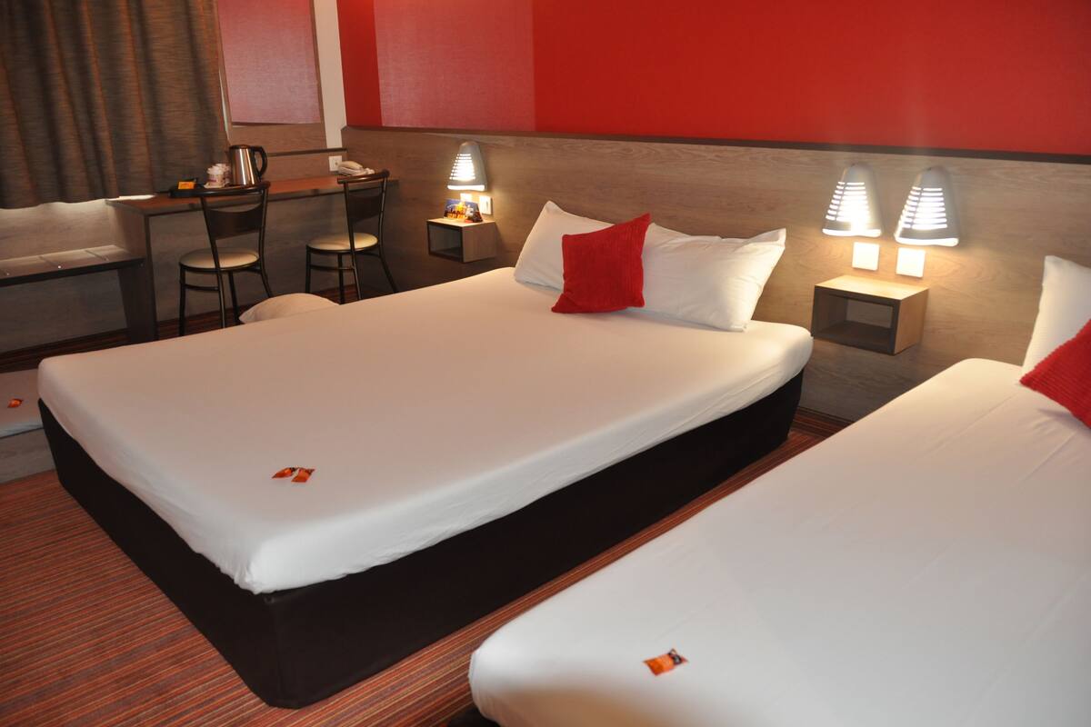 Une chambre d’hôtel avec deux lits, un bureau, des chaises et des lampes de chevet.